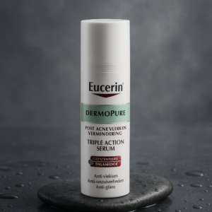 A premium studio shot of Eucerin Dermopure Sérum Triple Action 40ml, elegantly positioned on a sleek, wet stone surface that evokes purity and freshness. The product is well-lit with soft studio lighting, creating a gentle reflection and a subtle mist effect in the background. The packaging must match the exact brand and design details, ensuring fidelity to its typography and color scheme. Depth of field is short, focusing on the brand name with precision. The atmosphere is high-end and editorial, suiting a luxury health magazine.
